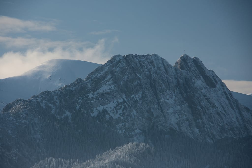 Thrilling Epic Christmas 2025 Murzasichle Tatra Adventures: Jagged rocky Tatra peaks rise dramatically through misty blue haze above frosted pine forests under moody winter skies in Poland.