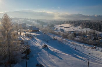 Aerial drone shot of Thrilling Epic Christmas 2025 Murzasichle Tatra Adventures: Snow-dusted wooden chalets and frosted pines dot a vast white valley, fresh ski tracks gleam under golden sunrise light on distant Tatra peaks Thrilling Epic Christmas 2025 Murzasichle Tatra Adventures
