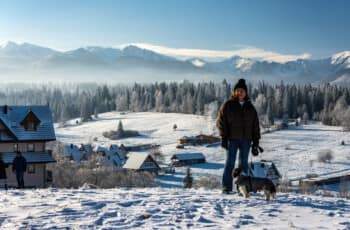 Thrilling Epic Christmas 2025 Murzasichle Tatra Adventures: Dorota with Monty stands on a snowy hill overlooking wooden chalets, frosted forests, and majestic Tatra peaks under blue skies. Dorota with Monty stands on a snowy hill overlooking wooden chalets