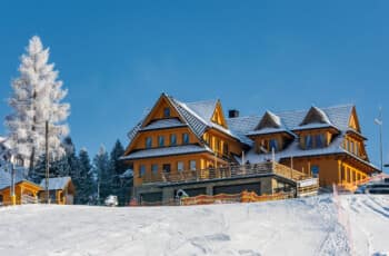 Thrilling Epic Christmas 2025 Murzasichle Tatra Adventures: Golden wooden chalet with snow-capped roofs stands proudly amid frosted pines and ski slopes under vivid blue skies. Golden wooden chalet with snow-capped roofs