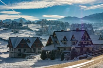 Thrilling Epic Christmas 2025 Murzasichle Tatra Adventures: Cluster of snow-roofed wooden chalets glows golden under blue skies and wispy clouds, rolling white hills and majestic Tatra peaks beyond Cluster of snow-roofed wooden chalets glows golden under blue skies and wispy clouds