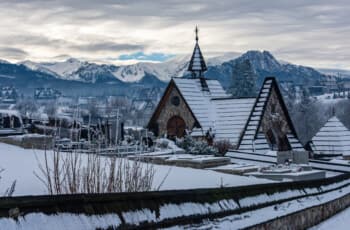 Thrilling Epic Christmas 2025 Murzasichle Tatra Adventures: Snowy Gothic chapel with steeple overlooks cemetery under cloudy skies, majestic Tatra peaks rising beyond in Poland's winter highlands Snowy Gothic chapel with steeple overlooks cemetery under cloudy skies